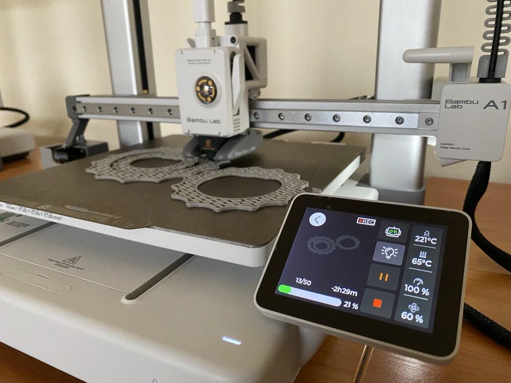 Impressora 3D Bambu Lab A1 com tela ligada durante a impressão de engrenagens